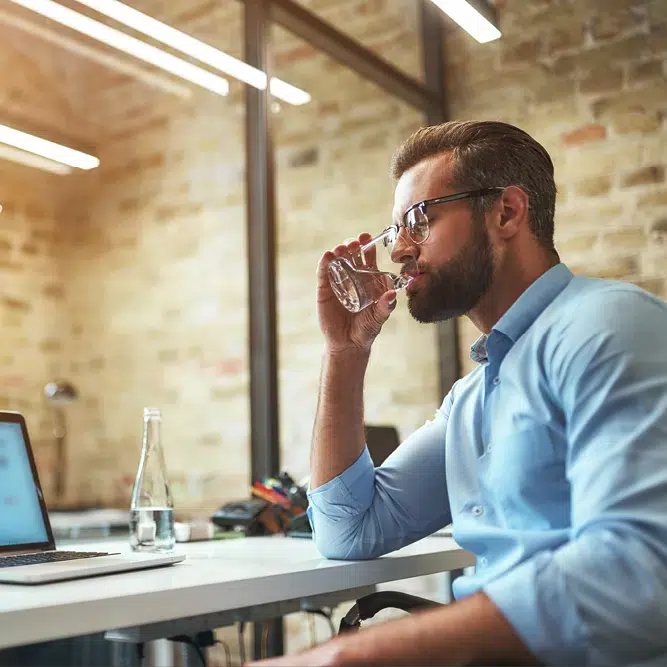 Man die van een fris glas water drinkt op zijn werk